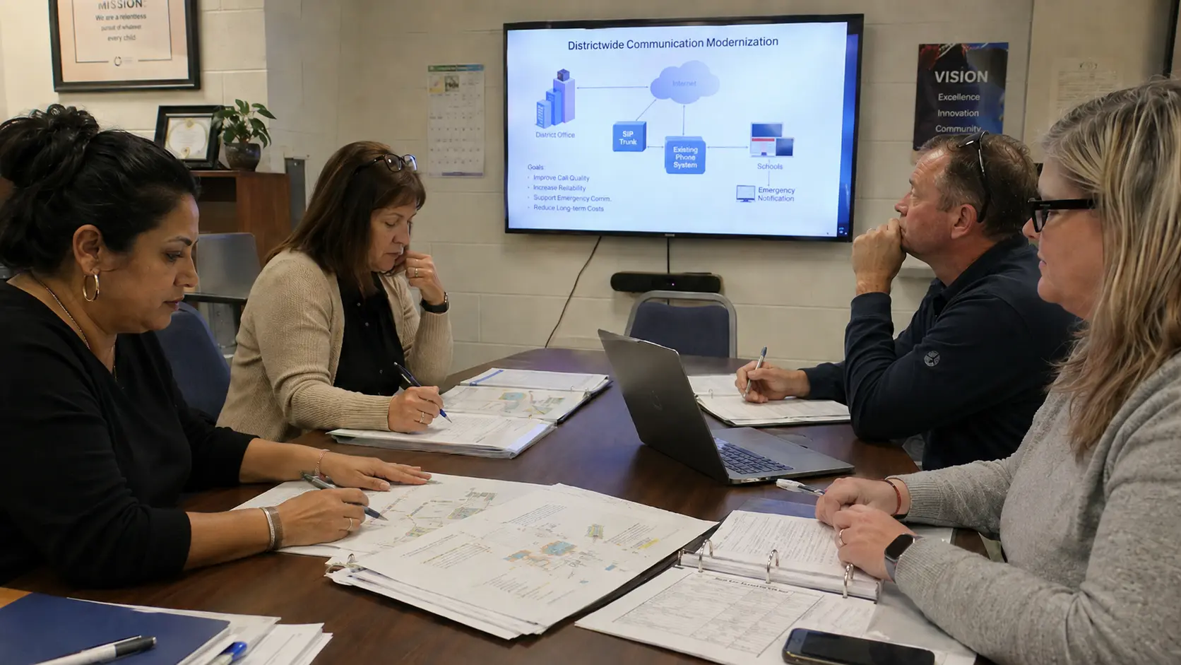 District leaders reviewing a phone system modernization plan in a school district meeting room.